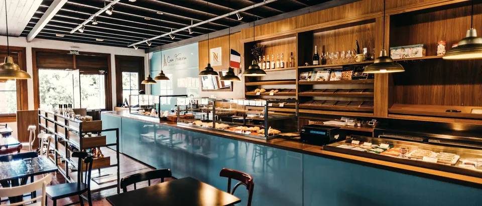Lange Cafétheke mit Auslagen und Vitrinen, davor Tische mit Stühlen.