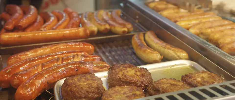 Grillplatte an einem Imbiss mit Bratwürsten und Frikadellen in Edelstahlschalen.